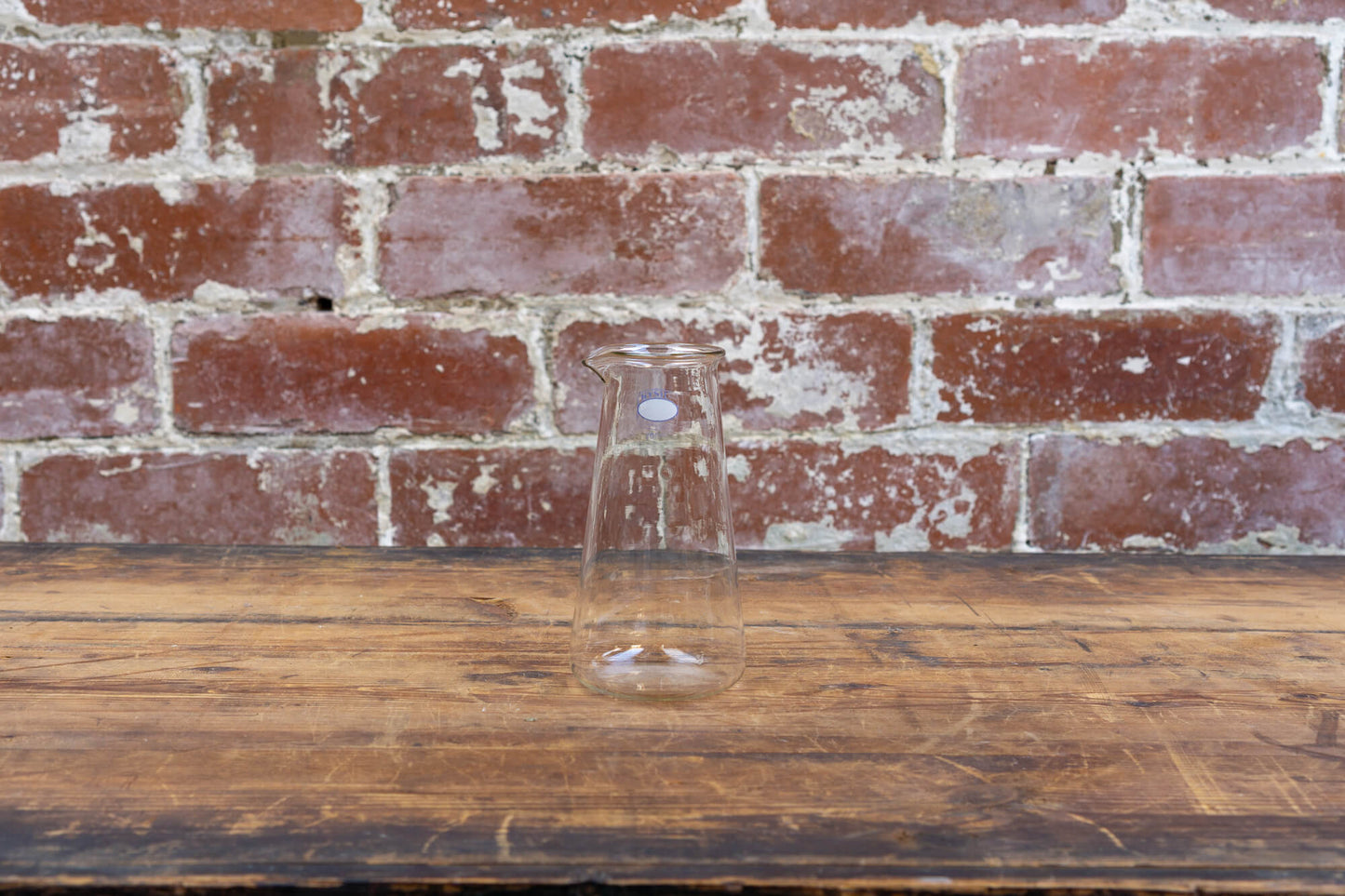 Photo shows a selection of vintage glass laboratory vessels on a table. The background is a red rustic brick wall.