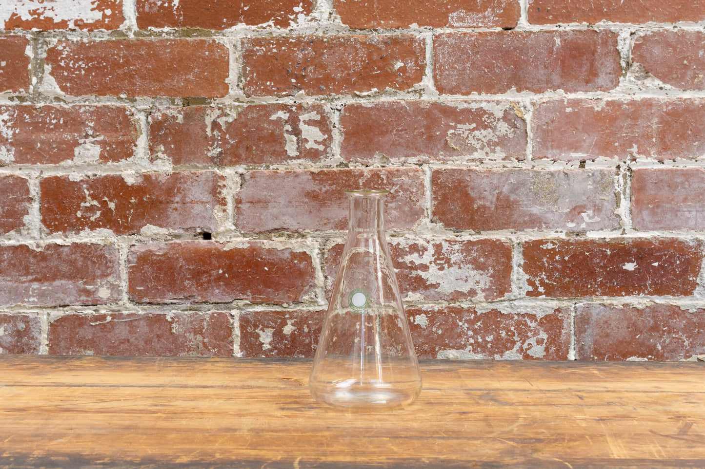 Photo shows a selection of vintage glass laboratory vessels on a table. The background is a red rustic brick wall.