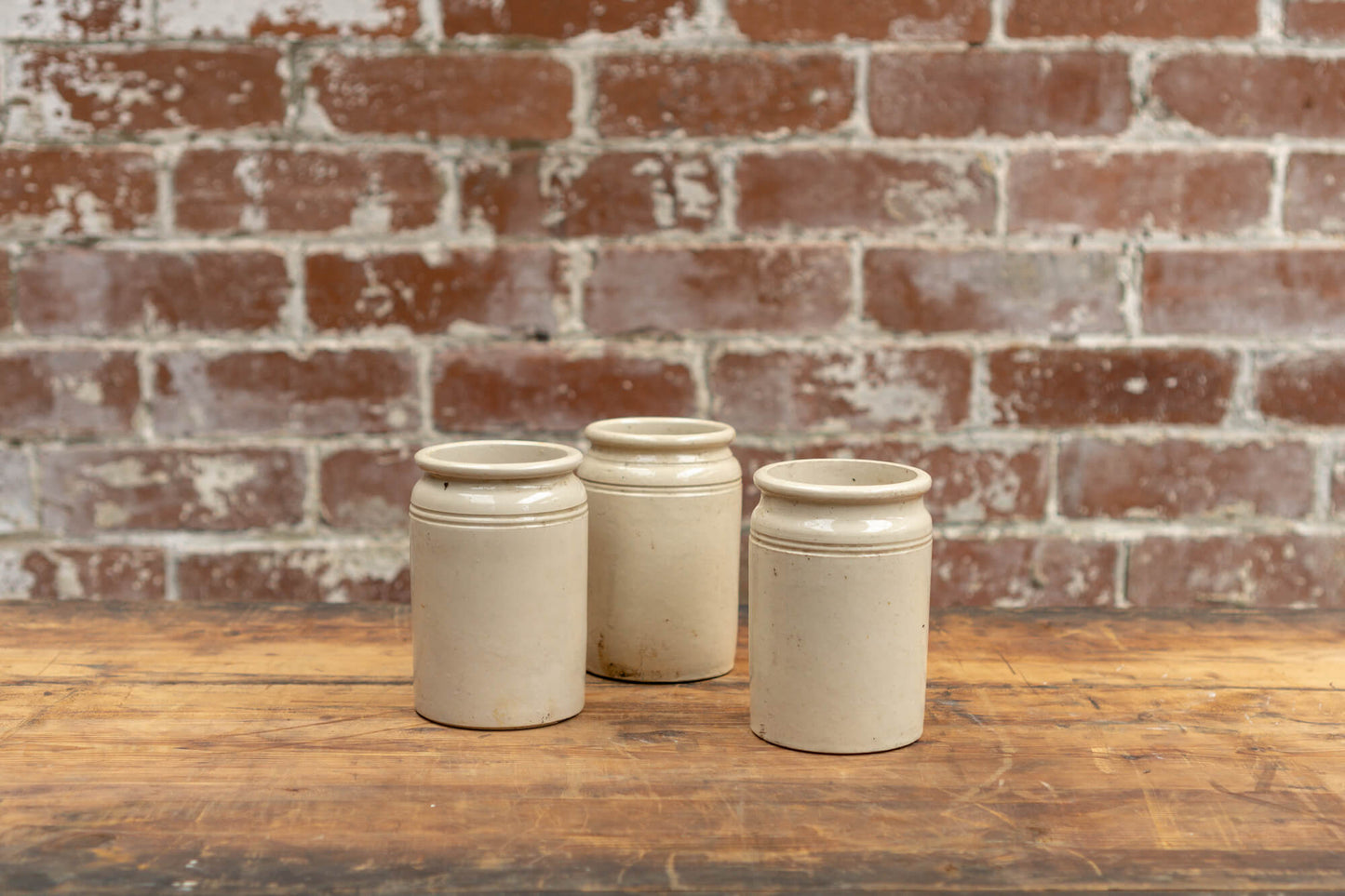 Photo shows 3 various sized salvaged Victorian stoneware jam conserve jars against a brick wall background. The jars are cream coloured with a glaze.