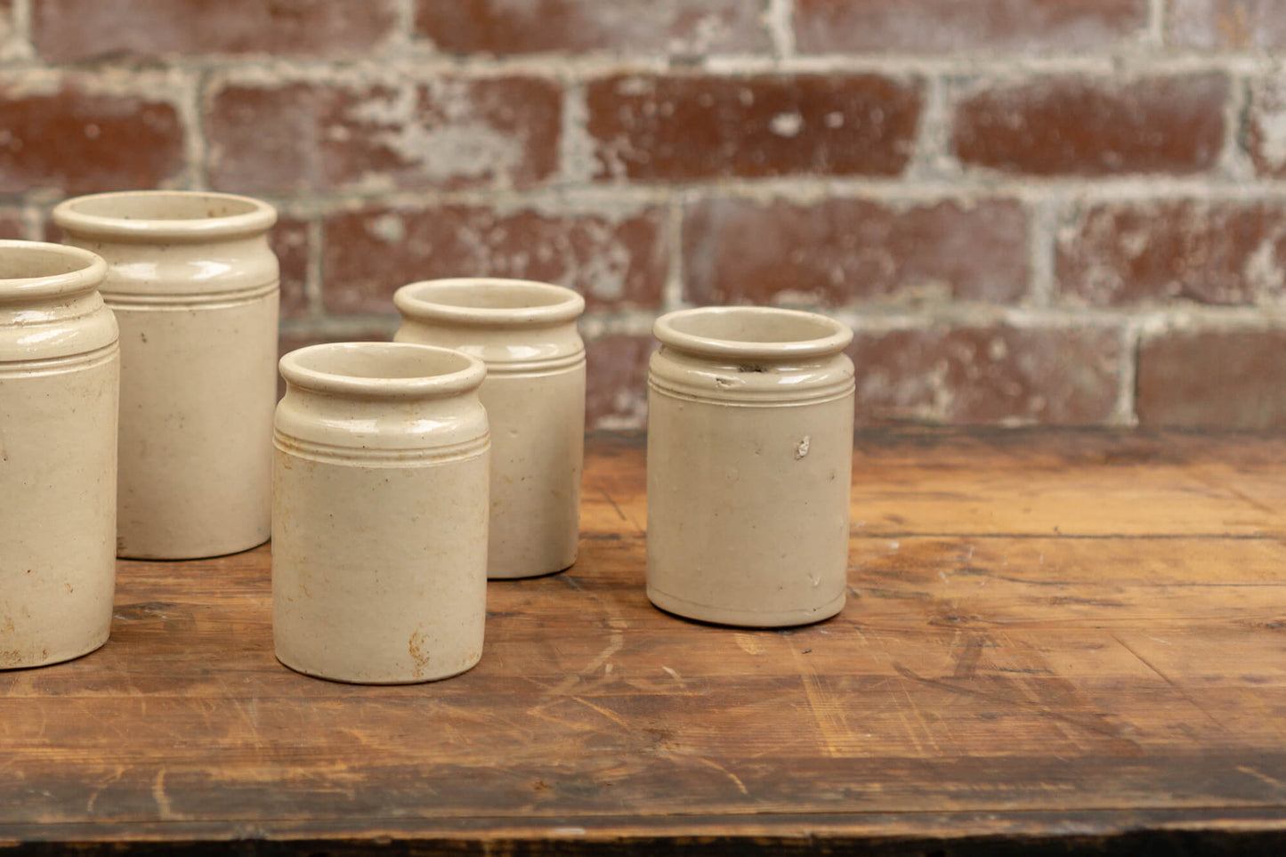 Photo shows 3 various sized salvaged Victorian stoneware jam conserve jars against a brick wall background. The jars are cream coloured with a glaze.
