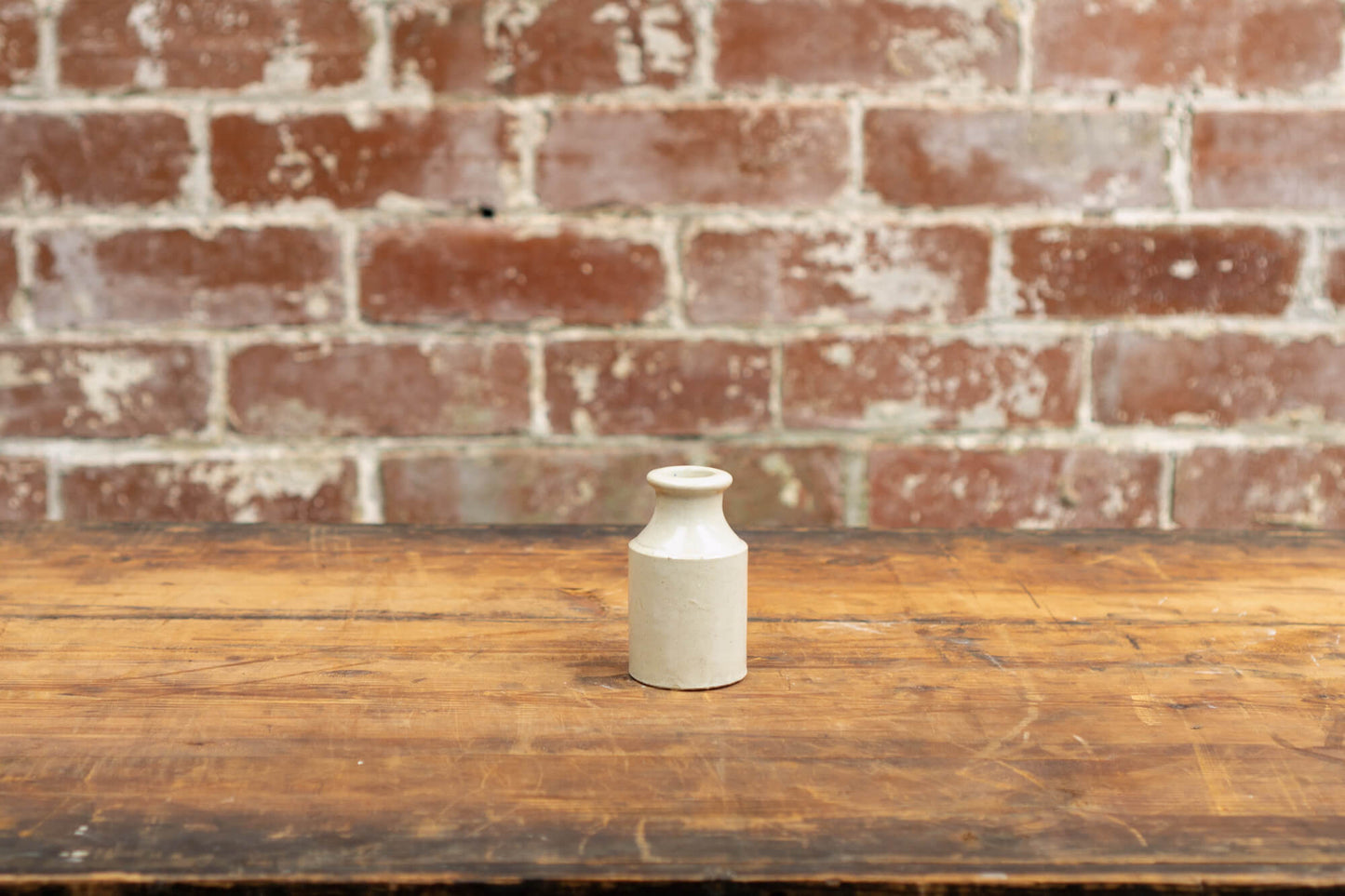 Image shows a collection of victorian stoneware bottles in shades of ivory, displayed neatly against a red brick wall backdrop