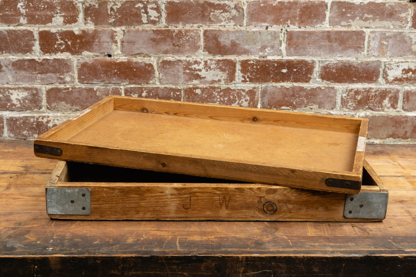Photo shows a vintage selection of wooden seed trays atop a table. The background is a red rustic brick wall.