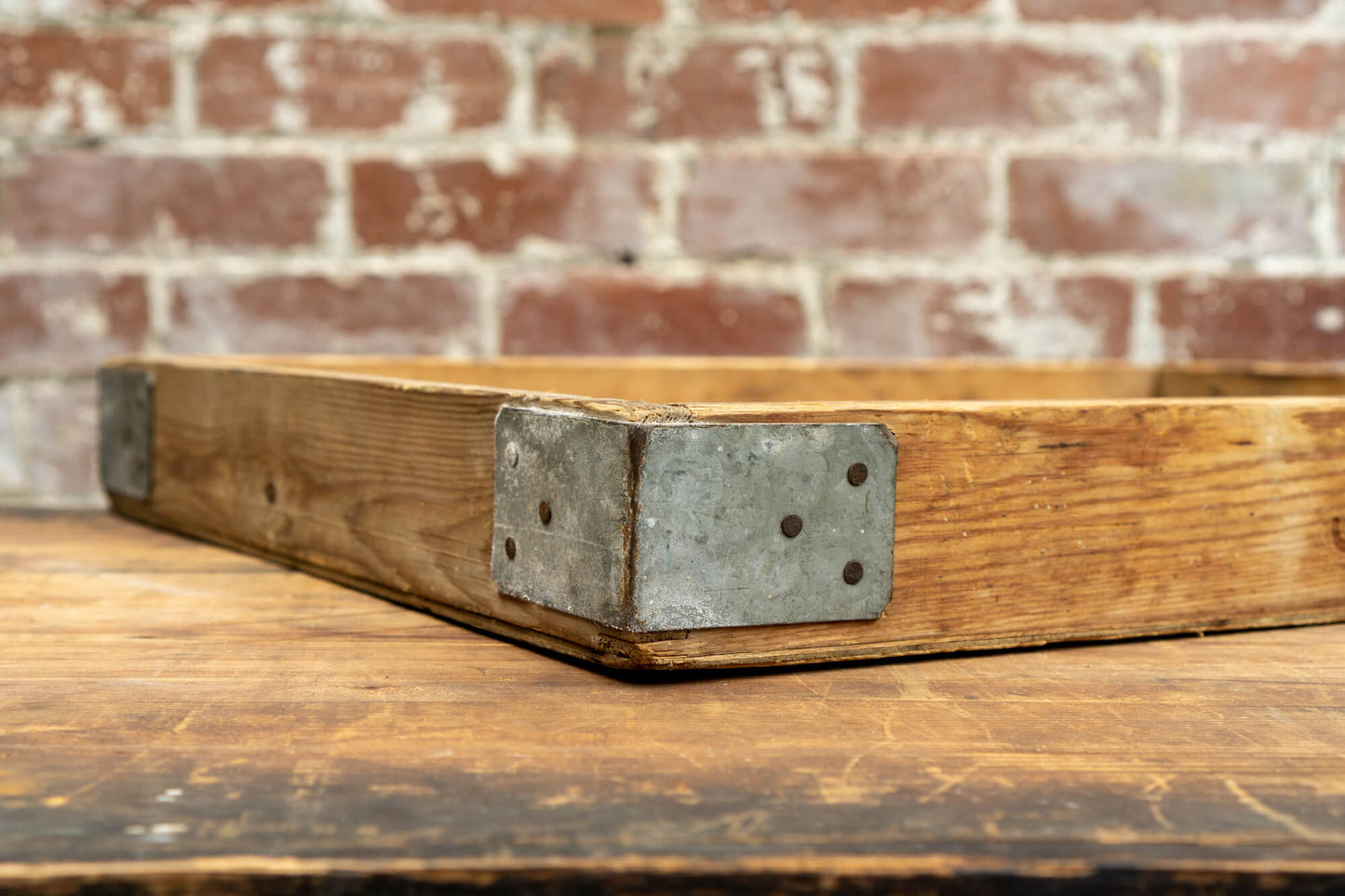 Photo shows a vintage selection of wooden seed trays atop a table. The background is a red rustic brick wall.